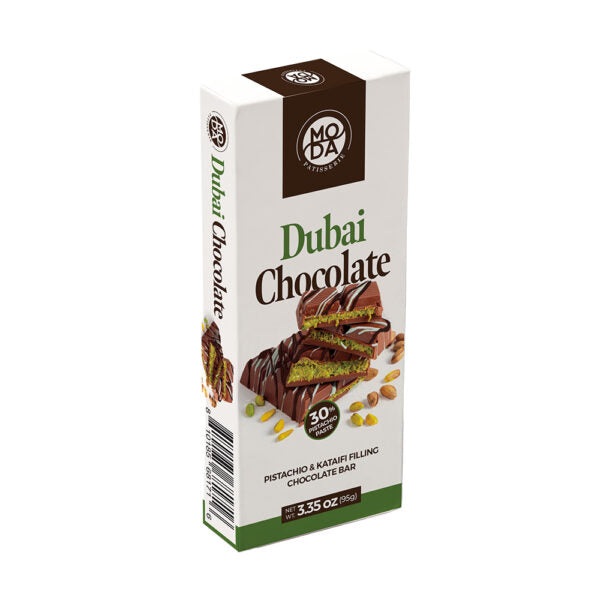 A boxed chocolate bar package labeled 'Dubai Chocolate' by Moda Confections, shown upright on a plain white background. The box is mostly white with brown and green branding and a photo of a chocolate bar with pistachio and kumquat filling on the front.