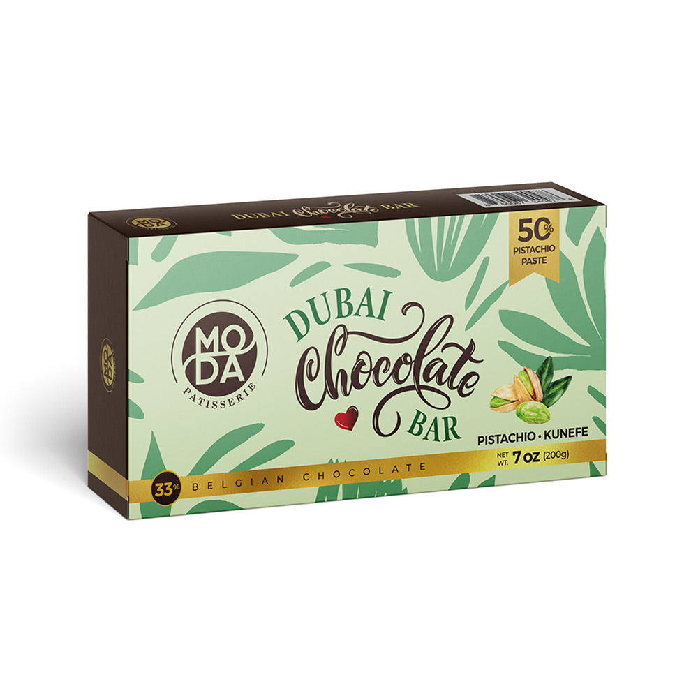 A box of Moda Belgian Chocolate Dubai Chocolate Bar, featuring a light green tropical leaf pattern with dark brown accents and text, and a small pistachio and kunefe illustration on the front.