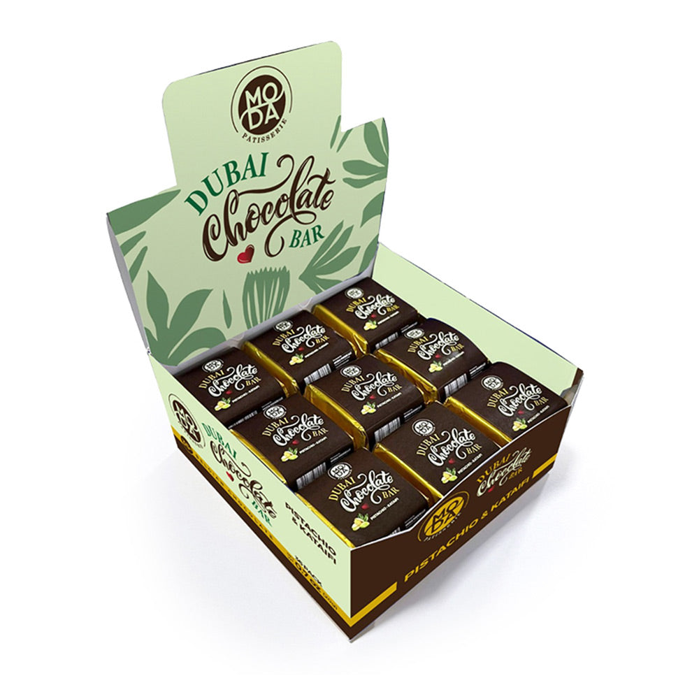 An open display box of Moda Chocolate Bar pistachio-flavored chocolate bars, showing multiple individually wrapped bars inside a branded green and brown carton on a white background.