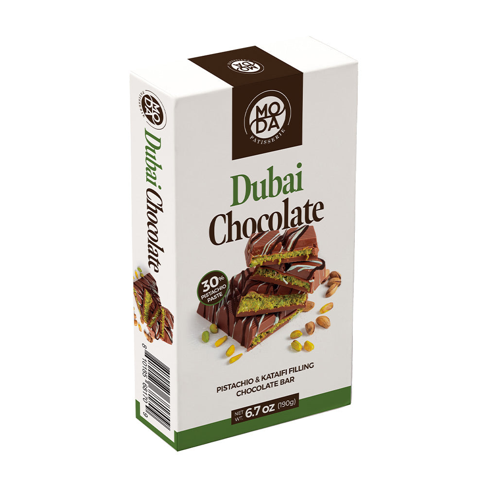 A boxed chocolate bar package labeled 'Dubai Chocolate' on a plain white background. The package is mostly white with dark brown and green branding and food photography showing a chocolate bar with pistachio pieces and a green cream filling.