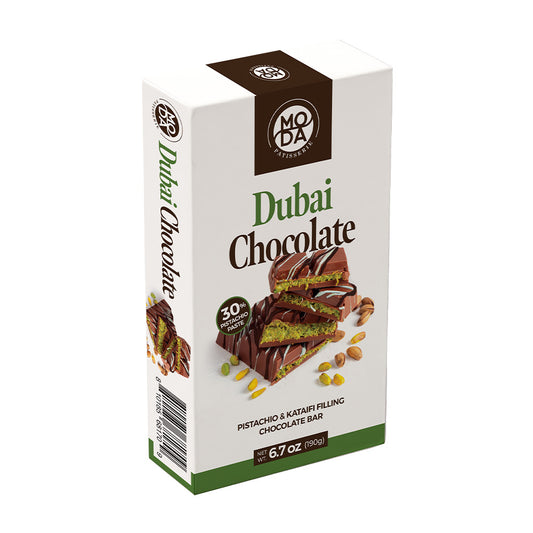 A boxed chocolate bar package labeled 'Dubai Chocolate' on a plain white background. The package is mostly white with dark brown and green branding and food photography showing a chocolate bar with pistachio pieces and a green cream filling.