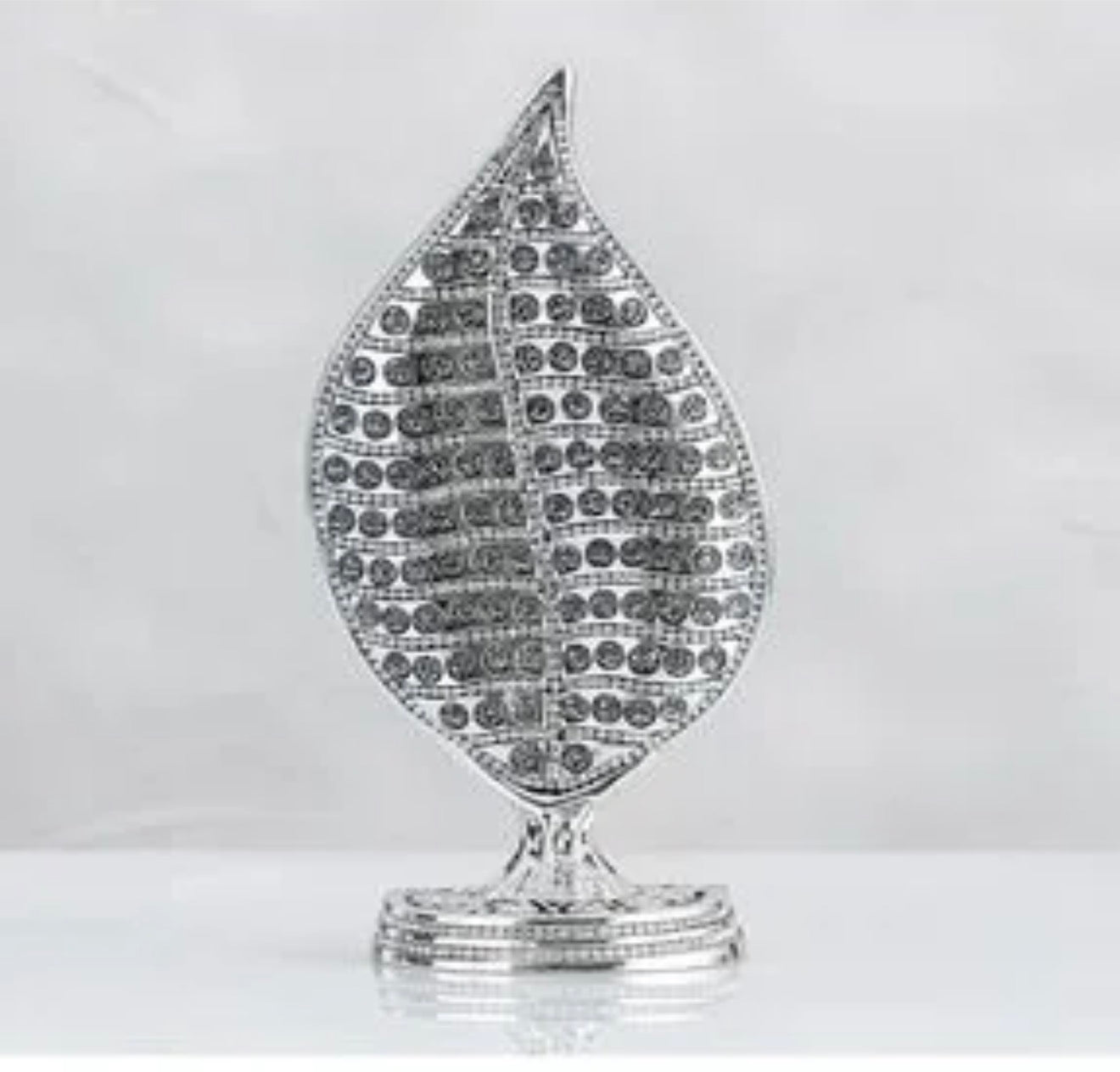 A silver-toned leaf-shaped decorative object with a textured, paved surface and a small matching base, shown against a light gray background.