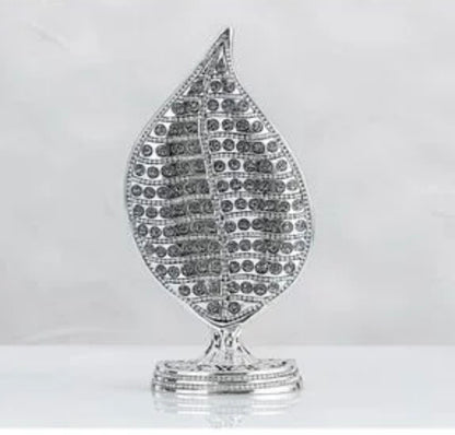 A silver-toned leaf-shaped decorative object with a textured, paved surface and a small matching base, shown against a light gray background.