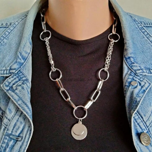 Person wearing a silver chain necklace with circular pendants, dressed in a denim jacket and black shirt.